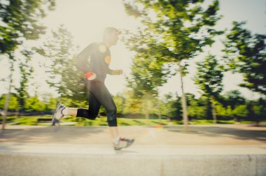 Hareket Bulanıklığı pratik spor aşırı arka plan ışığı mercek parlaması ile şehir Park'ta koşan genç adam görüntüsünü