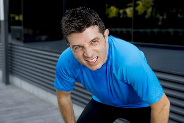 Young attractive man leaning exhausted after running session sweating taking a break to recover in urban street — Stock Photo, Image