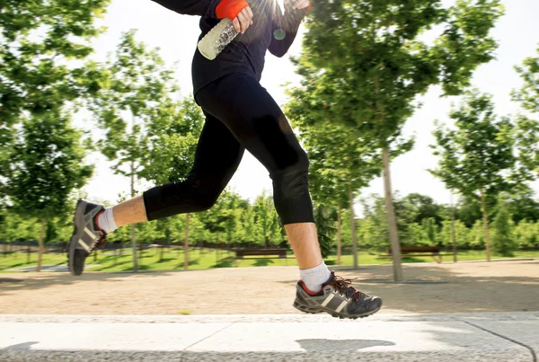 Close up legs of young man running in city park with trees on summer training session practicing sport healthy lifestyle concept — Stock Photo, Image