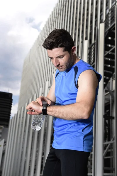 Junger Sportler überprüft Zeit auf Chrono-Timer-Läuferuhr mit Wasserflasche nach Trainingseinheit — Stockfoto