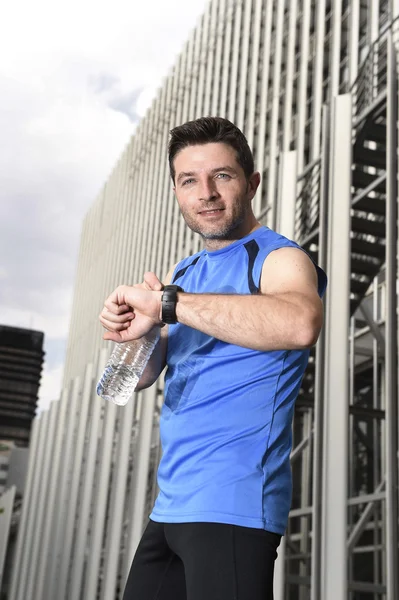 Joven hombre deportivo comprobar el tiempo en cronómetro corredores reloj celebración botella de agua después de la sesión de entrenamiento —  Fotos de Stock