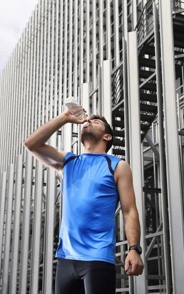 Young sport man drinking water bottle after running training session in business district — Stock Photo, Image
