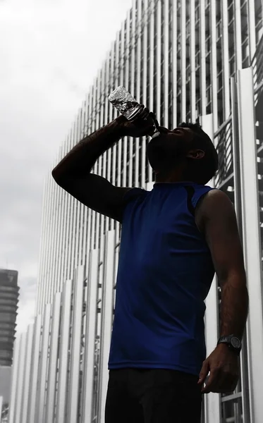 Silhouette of young sport man drinking water bottle after running training session in business district — Stock Photo, Image