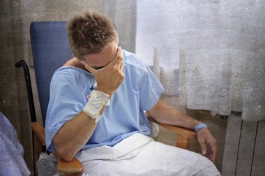 young injured man crying in hospital room sitting alone crying in pain worried for his health condition