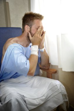 young injured man crying in hospital room sitting alone crying in pain worried for his health condition