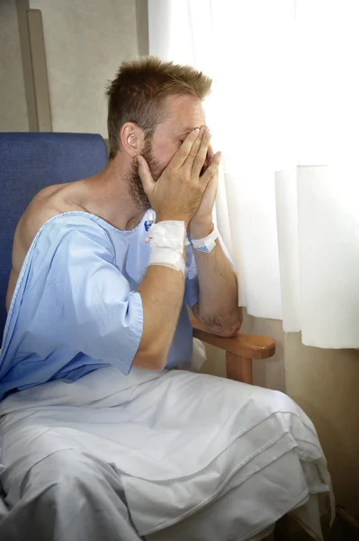 Young injured man crying in hospital room sitting alone crying in pain worried for his health condition — Stockfoto