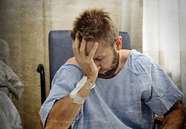 Young injured man in hospital room sitting alone in pain worried for his health condition — Stock Photo, Image