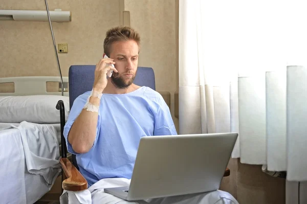 Young workaholic business man in hospital room sick and injured after accident working with mobile phone and computer laptop — Stockfoto