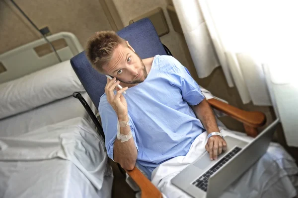 Молодой трудоголик-бизнесмен в больничной палате заболел и получил травму после аварии, работая с мобильным телефоном и ноутбуком — стоковое фото