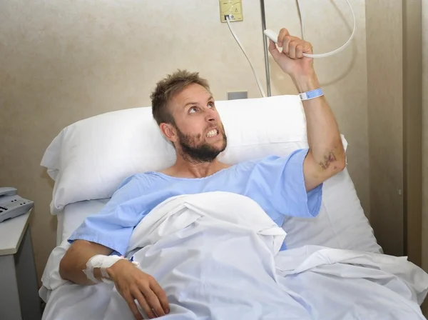 Сердитый пациент мужчина в больничной палате лежит в постели нажав кнопку вызова медсестры нервничает и расстроен — стоковое фото