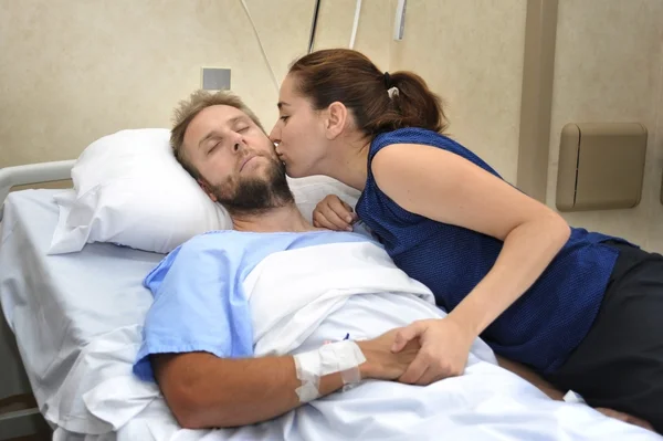 Joven pareja en hospital habitación hombre acostado en cama preocupado mujer sosteniendo su mano cuidado —  Fotos de Stock