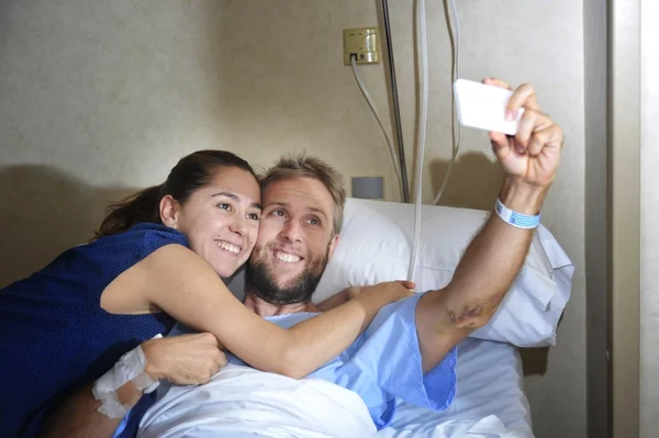 Jong koppel selfie foto nemen op ziekenhuis kamer met man in kliniek bed liggen — Stockfoto