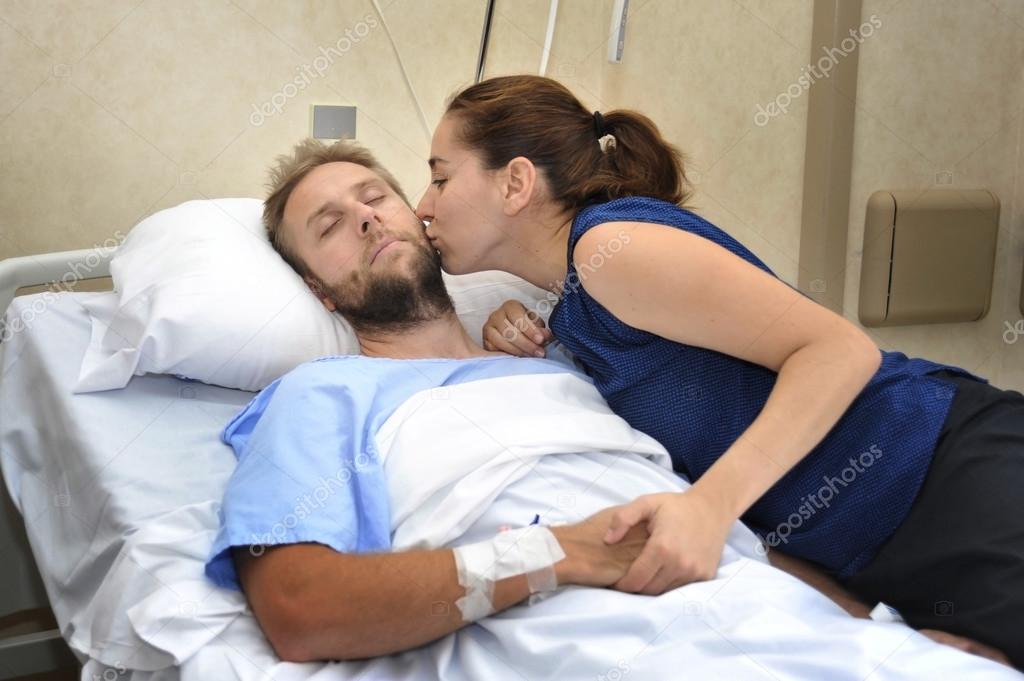 young couple at hospital room man lying in bed worried woman holding his hand caring