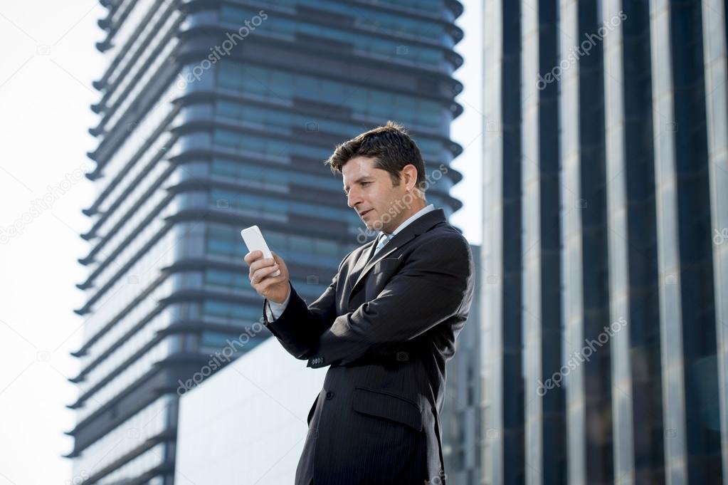 young attractive businessman in suit and necktie looking text message at mobile phone outdoors