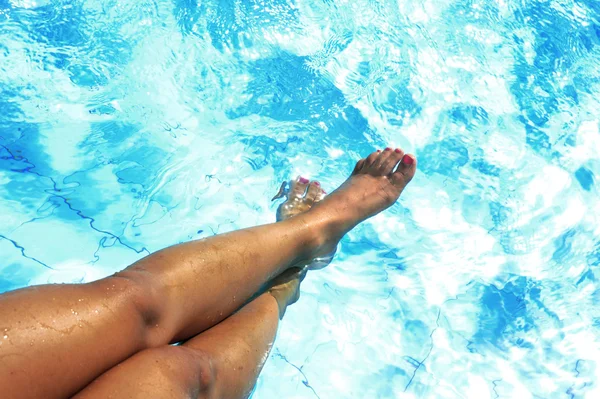 Tan golden legs of young woman and feet painted nails having suntan at swimming pool — Stock Photo, Image