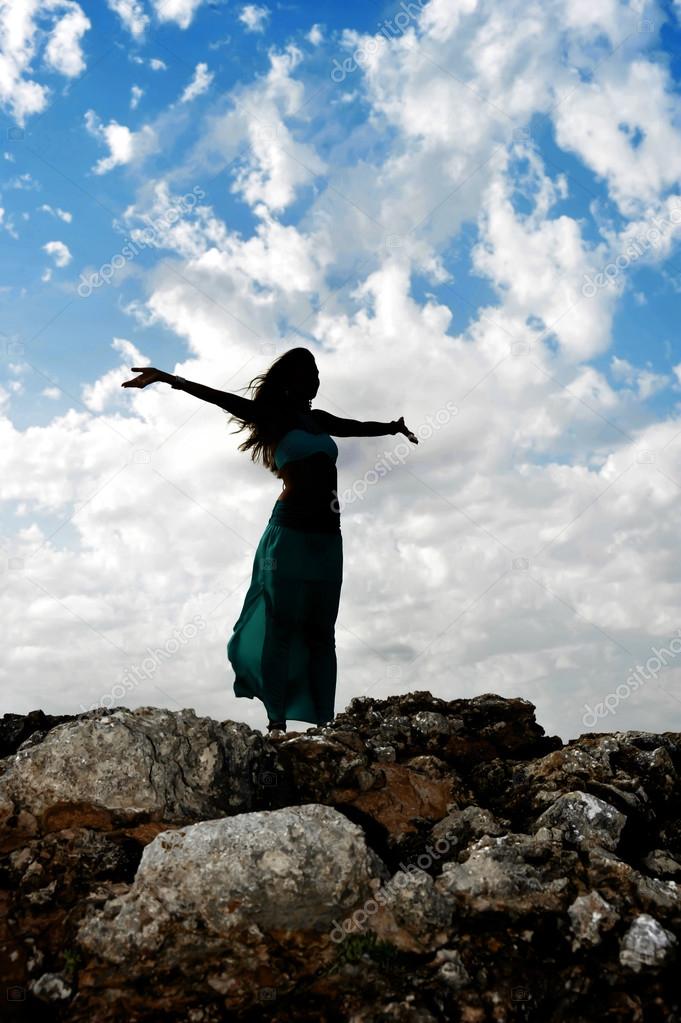 Silhouette of young attractive woman with opened arms outdoors i