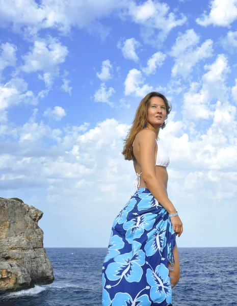 Mujer mirando el horizonte oceánico en el acantilado de roca por la orilla del mar en envoltura de playa sarong — Foto de Stock