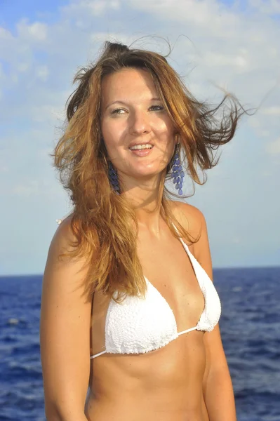 Attractive woman with hair moving with wind standing on beach in white bikini smiling happy — Stock Photo, Image