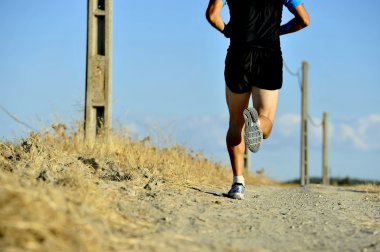 back view of young sport man legs and feet running on countryside track with power line poles