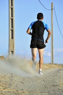 back view sport man running on countryside track with power line poles