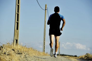 back view sport man running on countryside track with power line poles
