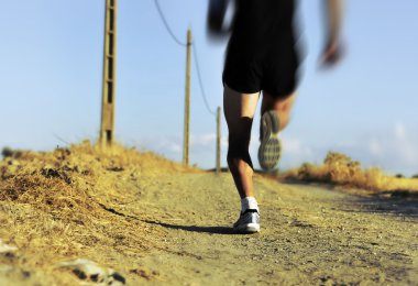 back view of young sport man legs and feet running on countryside track with power line poles