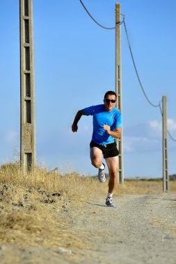 sport man with sun glasses running on countryside track with power line poles
