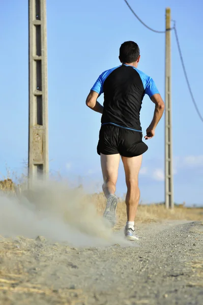 Back view homem do esporte correndo na pista rural com postes de linha de energia — Fotografia de Stock