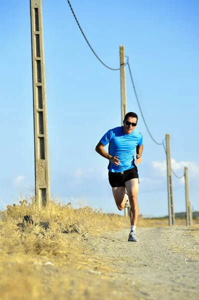 Sport man with sun glasses running on countryside track with power line poles — Stok fotoğraf