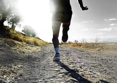 close up legs and feet of extreme cross country man running and training on rural track jogging at sunset