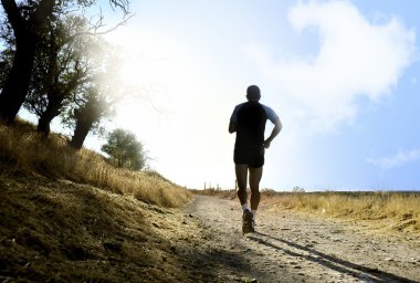 Silhouette of young sport man running on countryside in cross country workout at summer sunset