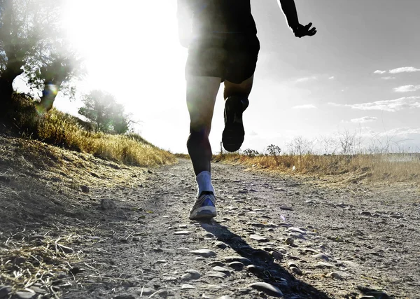 Close up legs and feet of extreme cross country man running and training on rural track jogging at sunset — Stockfoto