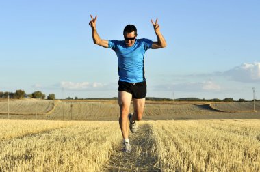 sport man running outdoors on straw field doing victory sign in frontal perspective