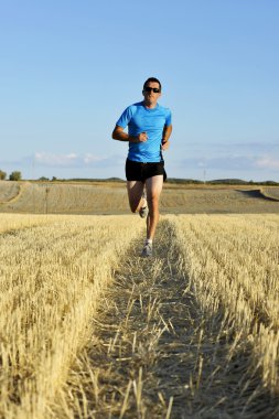 sport man with sunglasses running outdoors on straw field ground in frontal perspective