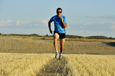 sport man with sunglasses running outdoors on straw field ground in frontal perspective