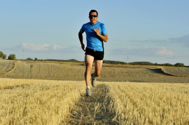 sport man with sunglasses running outdoors on straw field ground in frontal perspective