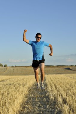 sport man running outdoors on straw field doing victory sign in frontal perspective