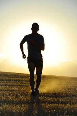 silhouette young sport man running off road in countryside straw field backlight at summer sunset