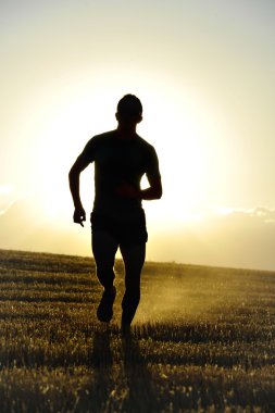 silhouette young sport man running off road in countryside straw field backlight at summer sunset