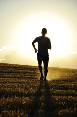 silhouette young sport man running off road in countryside straw field backlight at summer sunset