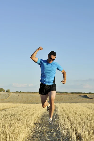 sport man running outdoors on straw field doing victory sign in frontal perspective