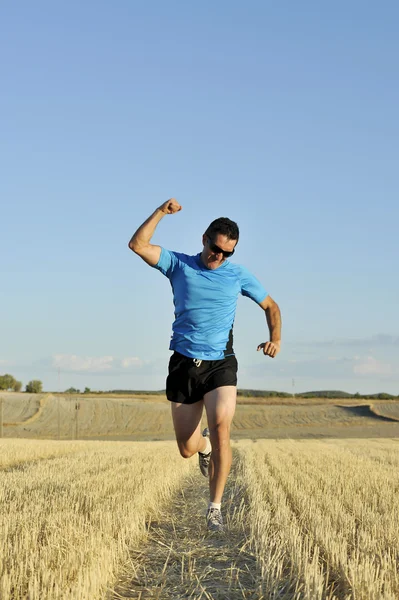 Sport man running outdoors on straw field doing victory sign in frontal perspective — Stok fotoğraf