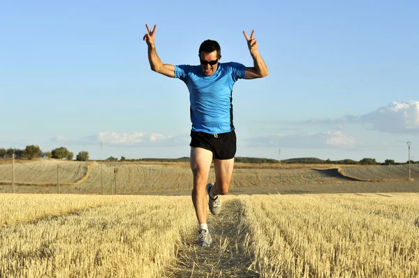 sport man running outdoors on straw field doing victory sign in frontal perspective