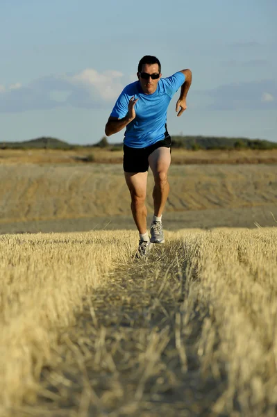 Sport man with sunglasses running outdoors on straw field ground in frontal perspective — Stok fotoğraf