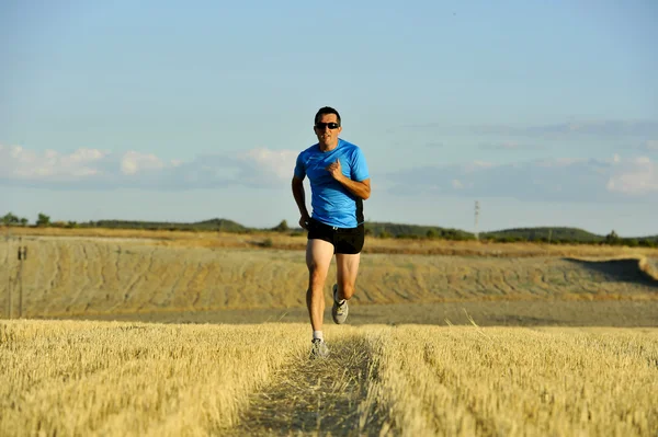 Hombre deportivo con gafas de sol corriendo al aire libre en el campo de paja en perspectiva frontal —  Fotos de Stock