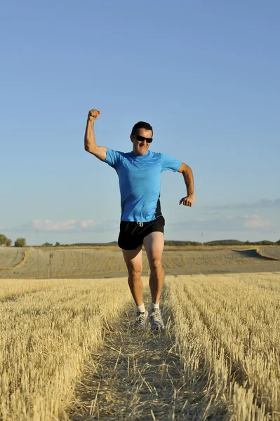 sport man running outdoors on straw field doing victory sign in frontal perspective