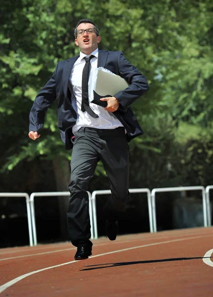 Businessman in suit and necktie carrying folder running desperate in stress on athletic track — Stock Photo, Image