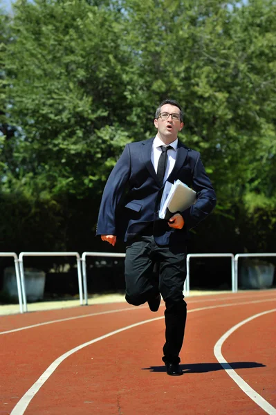 Businessman in suit and necktie carrying folder running desperate in stress on athletic track — Stock Photo, Image