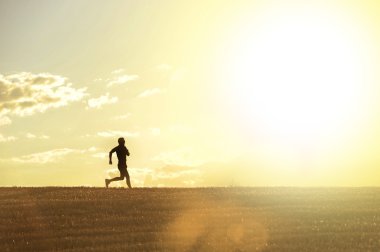 Profile silhouette of young man running in countryside training cross country jogging discipline in summer sunset on beautiful rural landscape