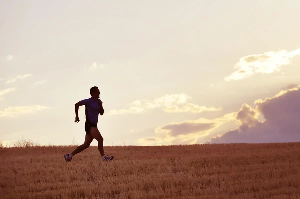Profile silhouette of young man running in countryside training in summer sunset — Stockfoto